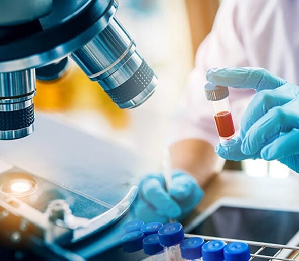 Close-up of a scientist's gloved hand holding a test tube with a blood sample, alongside a microscope and lab equipment, representing advanced medical research and laboratory diagnostics