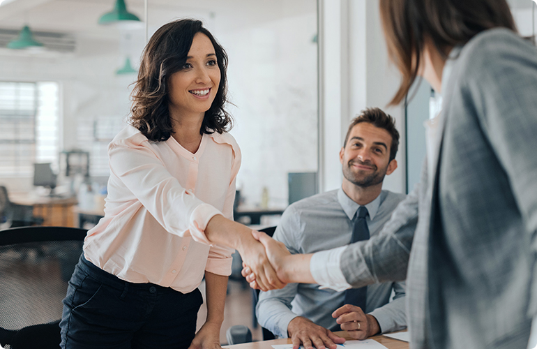 Smiling young businesswoman shaking hands with an office colleague